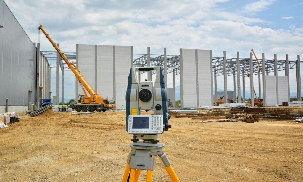 ALTA land survey equipment set up on construction site with cranes and structural framing in progress