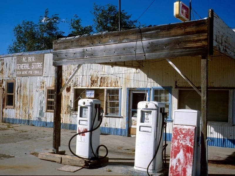 Old, weathered general store with corrugated metal siding and two vintage gas pumps under a wooden canopy.
